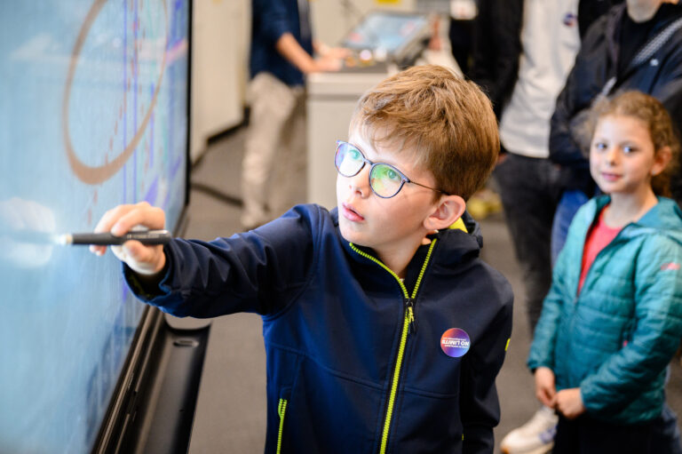 Ein junger Nachwuchsforscher malt mit einem Stift auf einen Bildschirm.