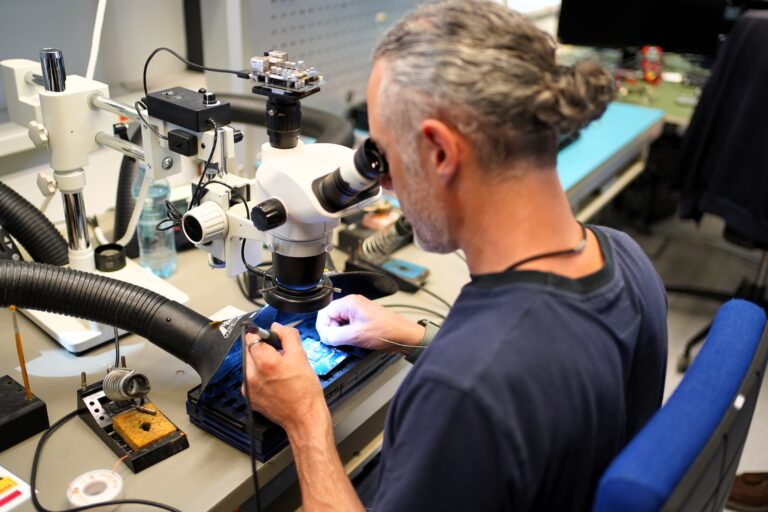 Mann lötet mit Mikroskop